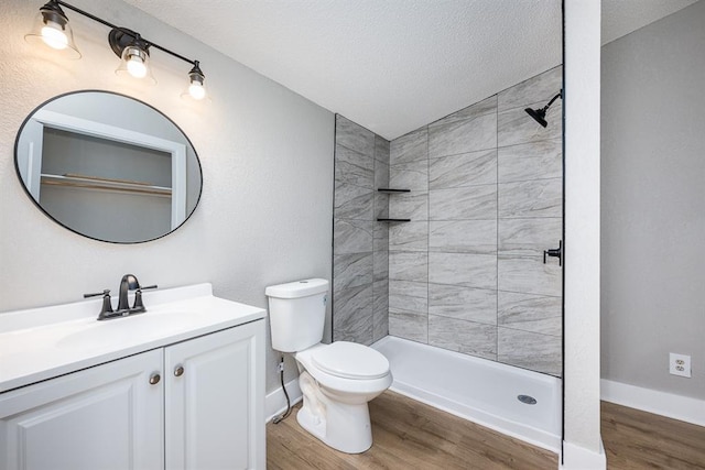 bathroom with a textured ceiling, hardwood / wood-style floors, vanity, tiled shower, and toilet