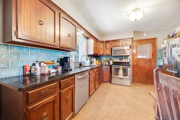 kitchen with backsplash, sink, appliances with stainless steel finishes, and dark stone counters