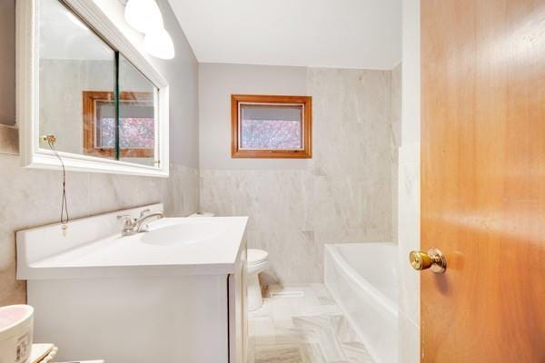 bathroom with vanity, a tub to relax in, toilet, and tile walls