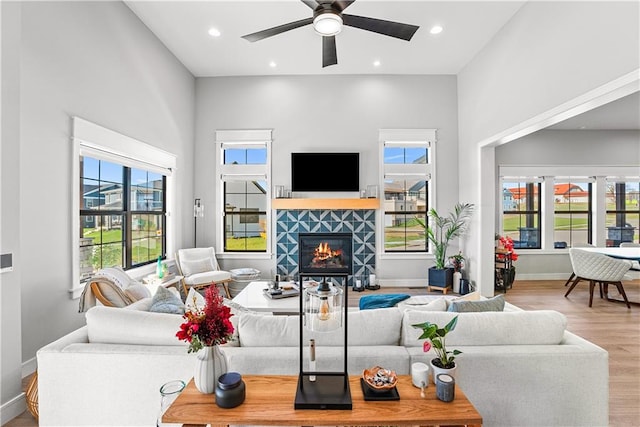 living room with a tiled fireplace, ceiling fan, light hardwood / wood-style flooring, and a towering ceiling