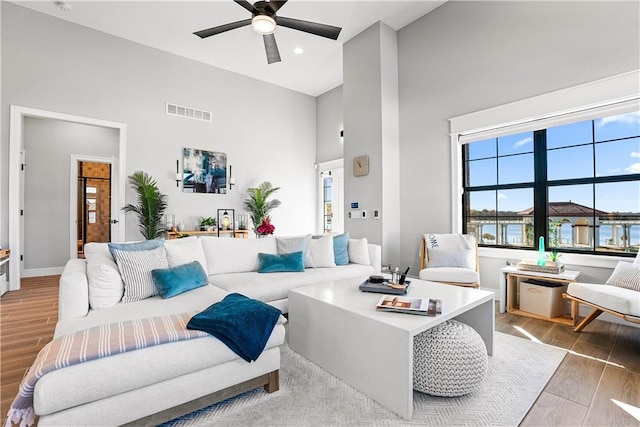 living room with ceiling fan, light hardwood / wood-style floors, a water view, and high vaulted ceiling