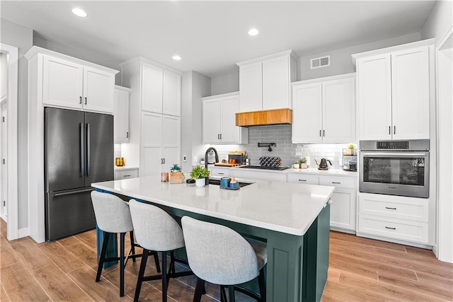 kitchen featuring a breakfast bar, a kitchen island with sink, light wood-type flooring, white cabinetry, and stainless steel appliances