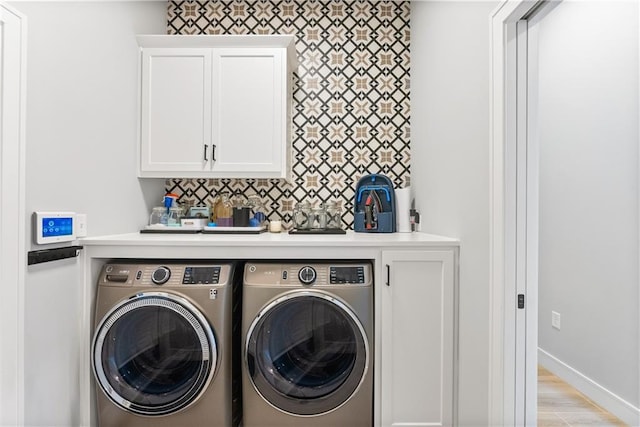 clothes washing area with washing machine and dryer, light hardwood / wood-style flooring, and cabinets