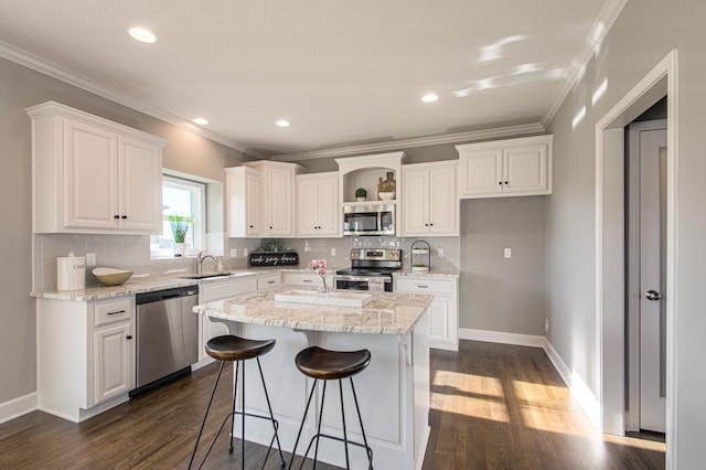 kitchen with dark wood finished floors, a sink, ornamental molding, stainless steel appliances, and white cabinetry