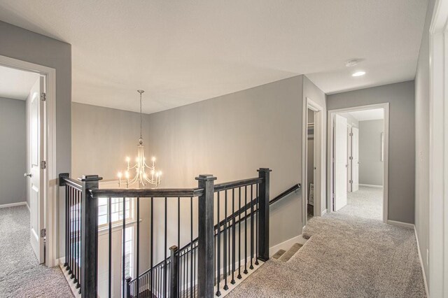 corridor featuring an inviting chandelier, an upstairs landing, baseboards, and carpet floors