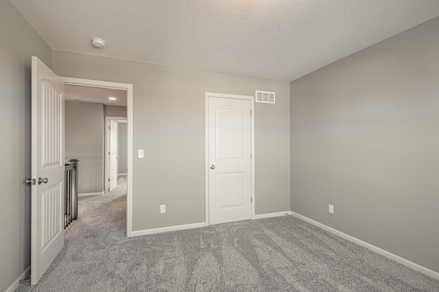 unfurnished bedroom featuring visible vents, a textured ceiling, baseboards, and carpet floors