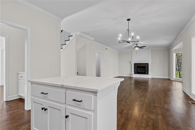 kitchen featuring a fireplace with raised hearth, dark wood-type flooring, pendant lighting, ornamental molding, and white cabinets