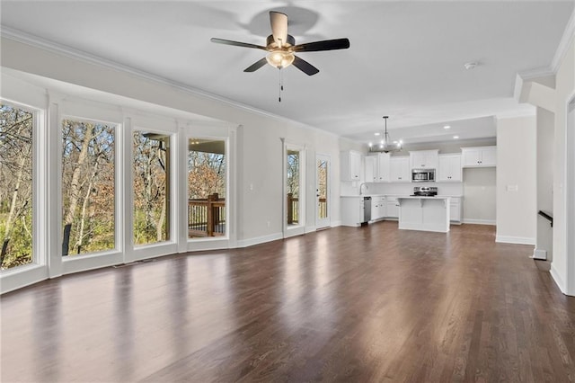 unfurnished living room featuring baseboards, dark wood-type flooring, ornamental molding, and ceiling fan with notable chandelier