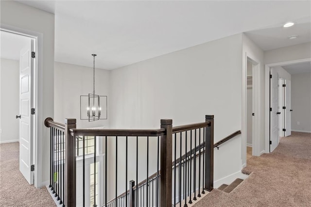 corridor featuring baseboards, carpet floors, an inviting chandelier, and an upstairs landing