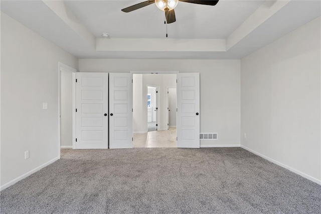 unfurnished bedroom featuring visible vents, a raised ceiling, and carpet floors