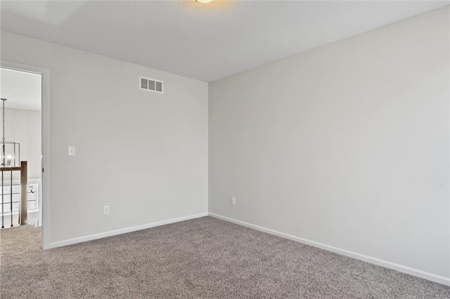 carpeted empty room featuring visible vents, baseboards, and a chandelier