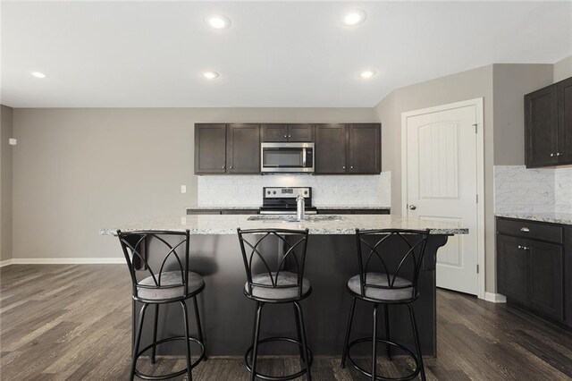 kitchen with a center island with sink, sink, dark hardwood / wood-style floors, appliances with stainless steel finishes, and tasteful backsplash