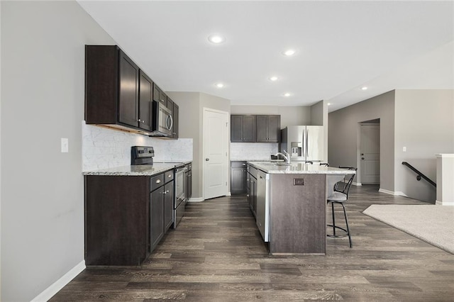 kitchen featuring appliances with stainless steel finishes, a breakfast bar area, dark wood-type flooring, and an island with sink