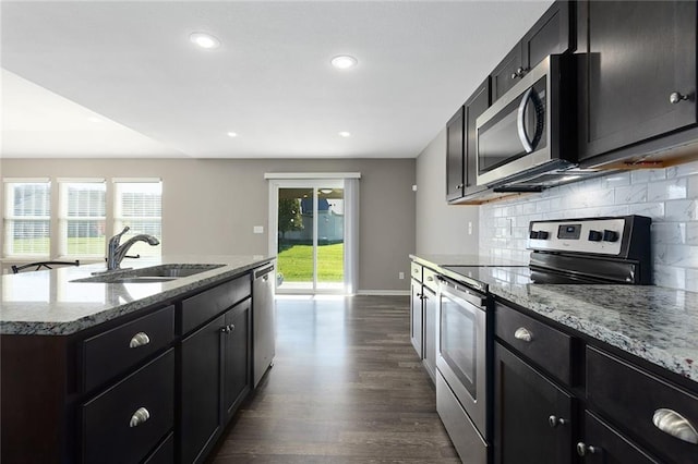 kitchen with appliances with stainless steel finishes, dark hardwood / wood-style flooring, backsplash, a kitchen island with sink, and sink