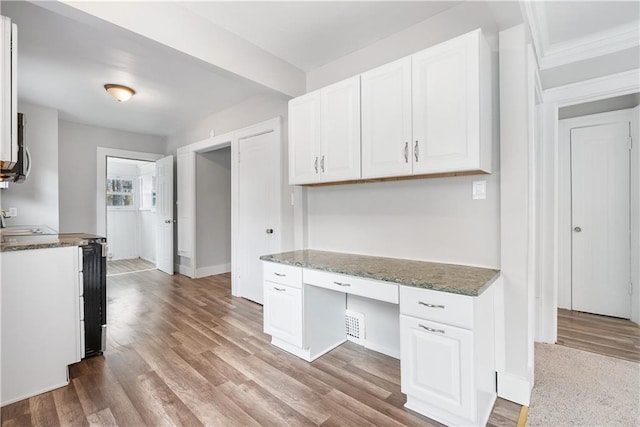 kitchen featuring white cabinets, built in desk, and light hardwood / wood-style flooring