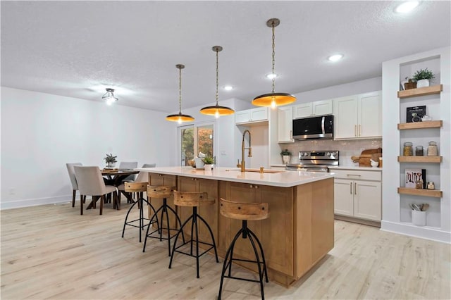 kitchen featuring light wood finished floors, a sink, light countertops, appliances with stainless steel finishes, and backsplash