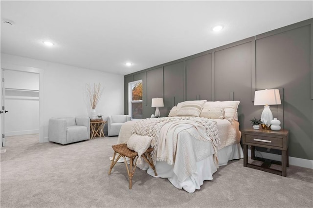 bedroom with a decorative wall, recessed lighting, light colored carpet, and baseboards