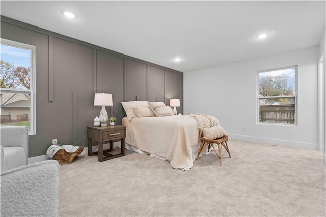 bedroom featuring recessed lighting, multiple windows, light carpet, and a decorative wall