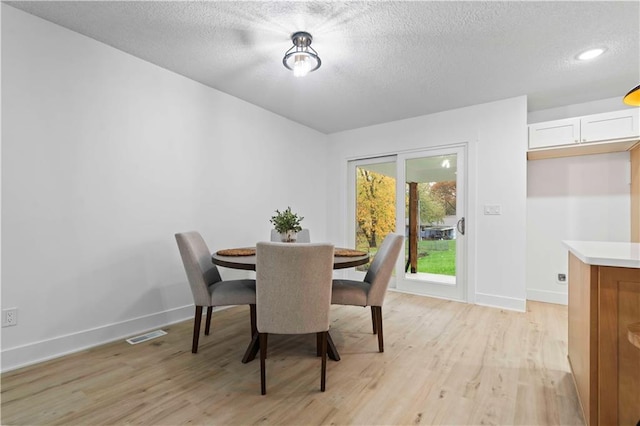 dining room featuring visible vents, baseboards, a textured ceiling, and light wood-style flooring