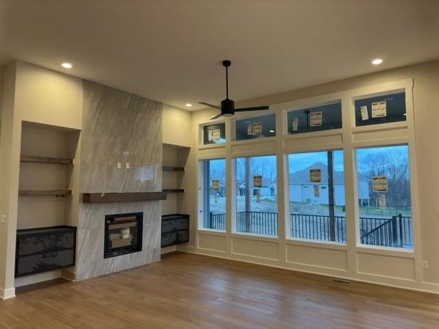 unfurnished living room featuring a high end fireplace, hardwood / wood-style flooring, built in features, and ceiling fan