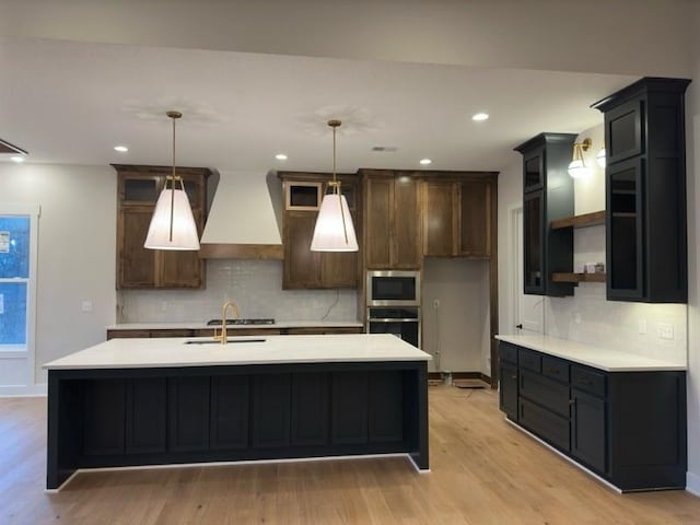 kitchen with custom range hood, dark brown cabinetry, light hardwood / wood-style flooring, and appliances with stainless steel finishes