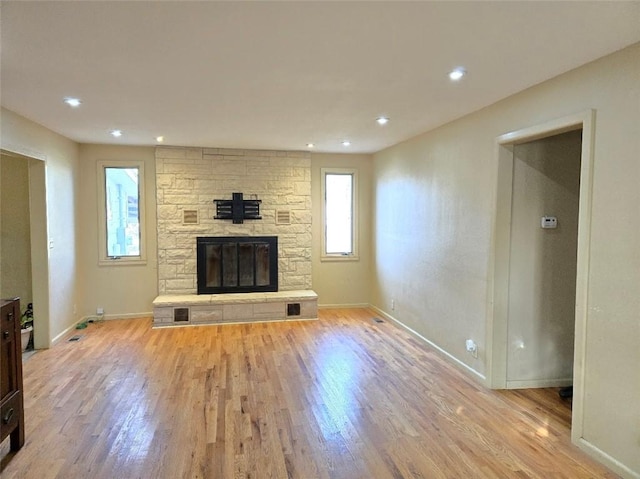 unfurnished living room featuring a stone fireplace and light wood-type flooring