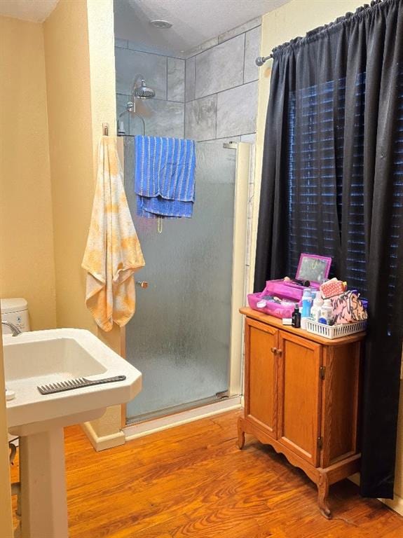 bathroom featuring toilet, wood-type flooring, a textured ceiling, and tiled shower