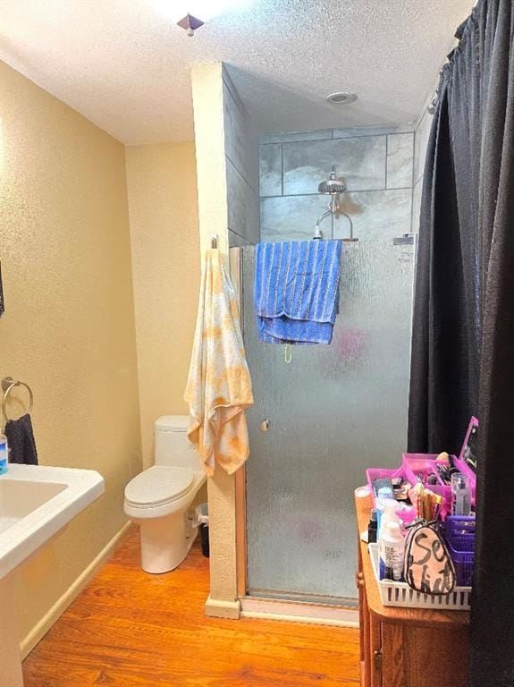 bathroom featuring toilet, a shower, wood-type flooring, and a textured ceiling