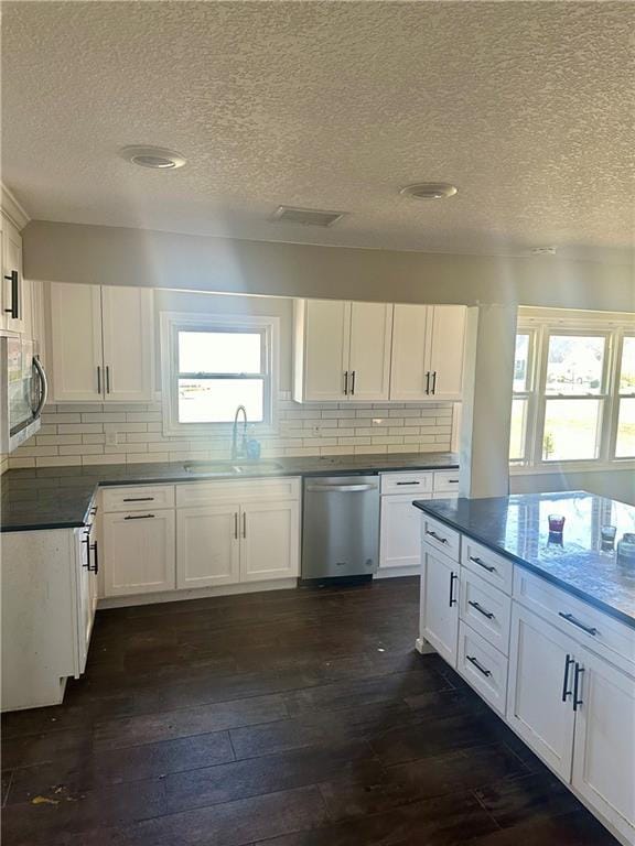 kitchen with appliances with stainless steel finishes, tasteful backsplash, a textured ceiling, white cabinets, and dark hardwood / wood-style flooring