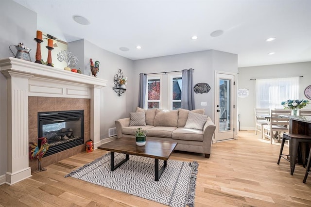 living room with a tiled fireplace, light wood-type flooring, and plenty of natural light