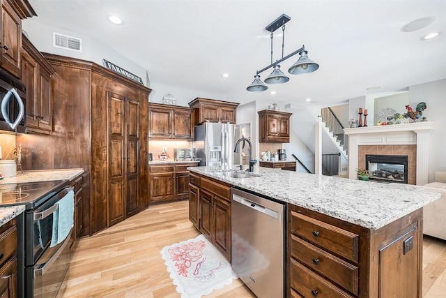 kitchen featuring a center island with sink, sink, pendant lighting, light wood-type flooring, and appliances with stainless steel finishes