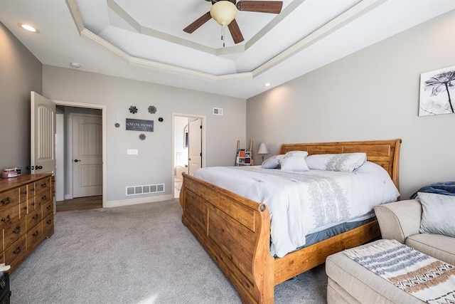 bedroom with a raised ceiling, light colored carpet, ceiling fan, and ensuite bath