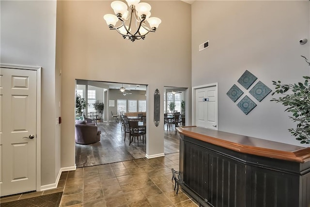 foyer entrance with hardwood / wood-style flooring, ceiling fan with notable chandelier, and a towering ceiling