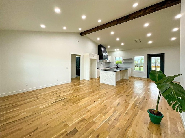 kitchen featuring light hardwood / wood-style floors, beamed ceiling, white cabinetry, a center island, and wall chimney range hood