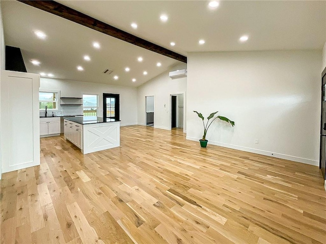 kitchen featuring light wood-type flooring, a wall mounted AC, vaulted ceiling with beams, and white cabinets