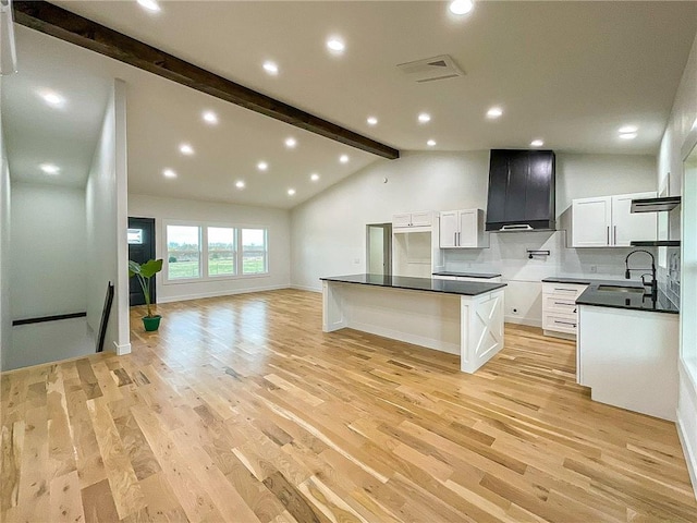 kitchen with beamed ceiling, wall chimney exhaust hood, a kitchen island, white cabinets, and light wood-type flooring