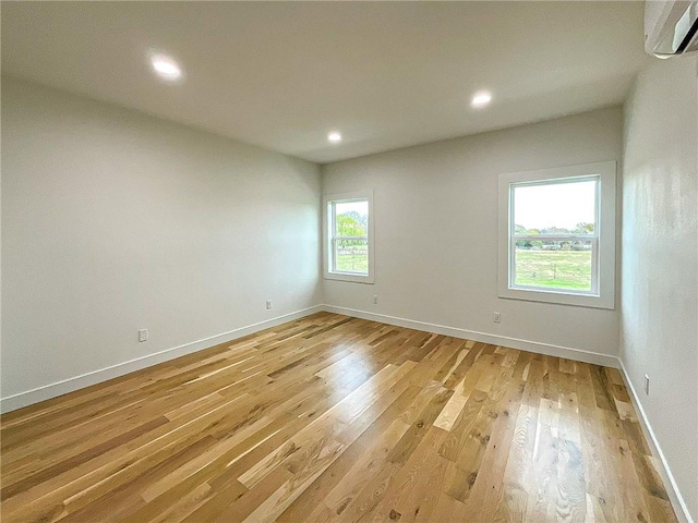 empty room with plenty of natural light, light hardwood / wood-style flooring, and a wall mounted air conditioner