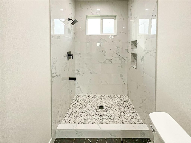 bathroom featuring tile patterned floors, toilet, and a tile shower