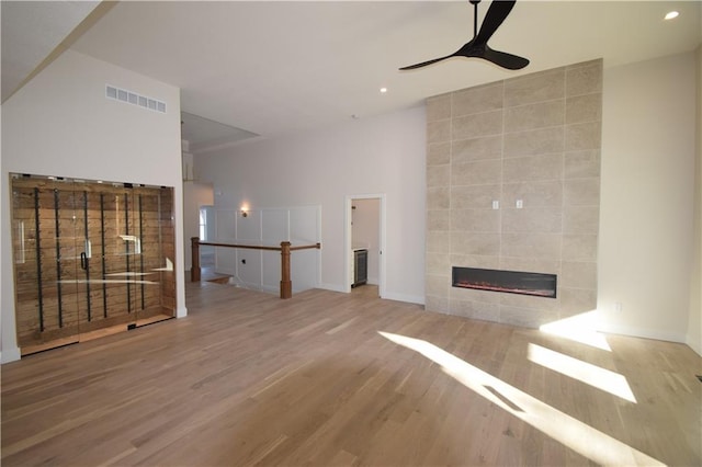 unfurnished living room featuring a tile fireplace, ceiling fan, and light hardwood / wood-style flooring