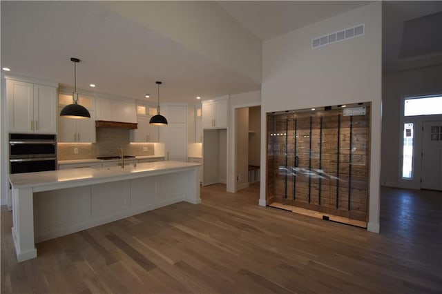 kitchen with hardwood / wood-style flooring, an island with sink, hanging light fixtures, and white cabinets