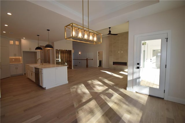 kitchen featuring pendant lighting, dishwasher, white cabinetry, a fireplace, and an island with sink