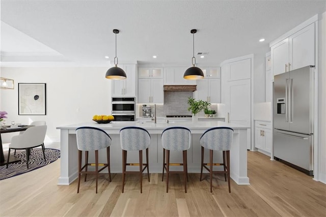 kitchen with tasteful backsplash, white cabinets, stainless steel appliances, and light countertops