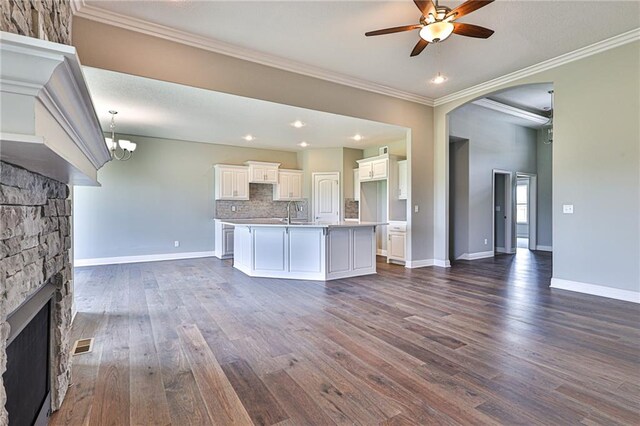 kitchen featuring ornamental molding, ceiling fan, backsplash, an island with sink, and dark wood-type flooring