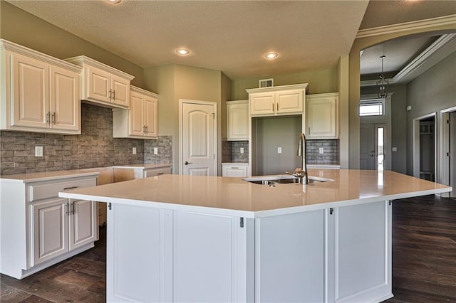 kitchen with tasteful backsplash, a textured ceiling, dark hardwood / wood-style floors, sink, and an island with sink