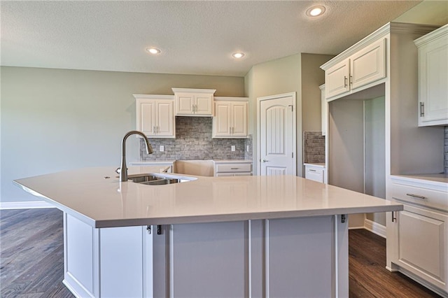 kitchen featuring white cabinetry, backsplash, dark hardwood / wood-style flooring, sink, and a kitchen island with sink