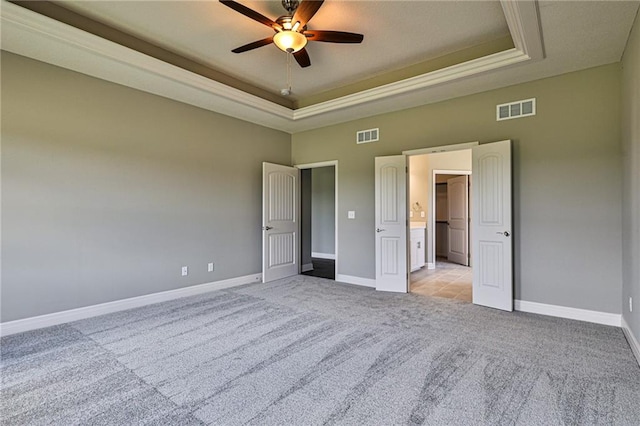 unfurnished bedroom with ceiling fan, light carpet, and a tray ceiling