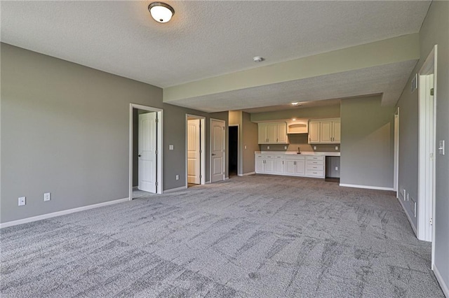 unfurnished living room with a textured ceiling, light colored carpet, and built in desk