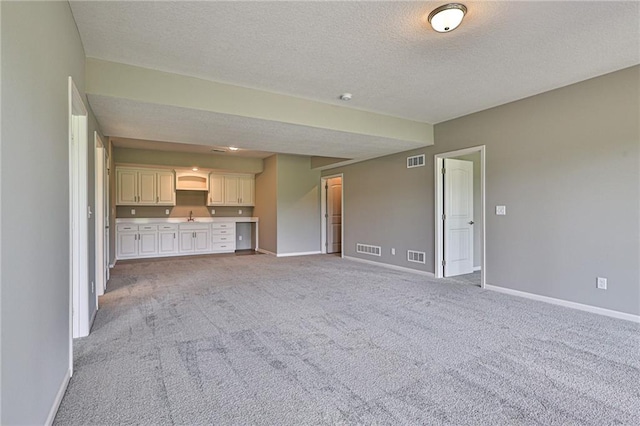 unfurnished living room with a textured ceiling, light carpet, and sink