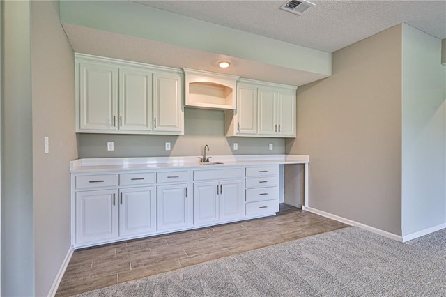 kitchen featuring white cabinets, light hardwood / wood-style flooring, a textured ceiling, and sink