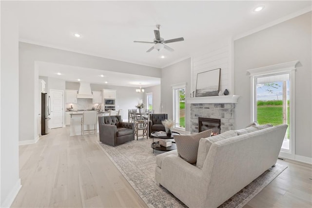 living room with a wealth of natural light, a stone fireplace, light wood-type flooring, and ornamental molding